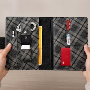 Puede incluir: Una funda para tableta a cuadros grises y negros con múltiples bolsillos y compartimentos. La funda está abierta, revelando un bloc de notas amarillo, una tableta negra y un tarjetero rojo. También son visibles accesorios como un lápiz óptico, un cable de carga y un bloque de carga blanco.