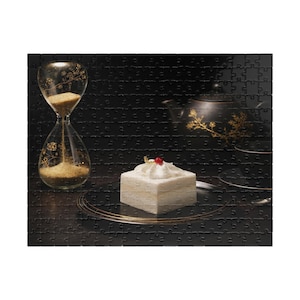 Könnte beinhalten: Ein Stillleben-Puzzle mit einem quadratischen weißen Kuchen mit roter Kirsche, einer goldfarbenen Sanduhr und einer schwarzen Teekanne mit goldenen floralen Designs. Die Objekte sind auf einer dunklen Oberfläche angeordnet und erzeugen eine elegante Ästhetik.