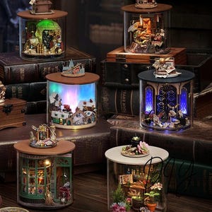 May include: A collection of miniature, illuminated scenes encased in glass jars. Each jar features a unique diorama with intricate details, including buildings, figures, and decorative elements. The jars have wooden lids and sit on a surface of antique books.