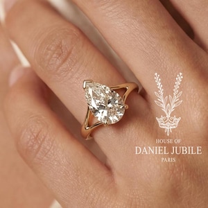 Könnte beinhalten: Ein goldener Ring mit einem birnenförmigen Diamanten. Der Ring befindet sich an einem Finger. Das Bild enthält den Text "HOUSE OF DANIEL JUBILE PARIS".