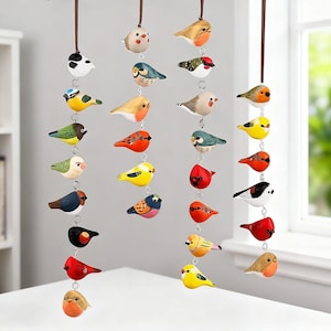 以下が含まれることがあります： 手描きの木製鳥のオーナメントのコレクション。赤、黄色、青など様々な色で、茶色の紐から吊り下げられています。各鳥は小さな金属リングで次の鳥に接続されています。