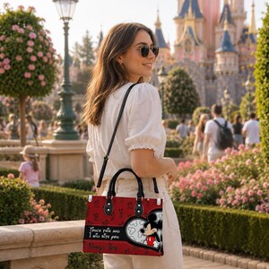 May include: A red rectangular handbag featuring a black Mickey Mouse graphic inside a white heart-shaped outline, black handles, and a black shoulder strap. The bag displays the text "Touch this and I will bite you" and "Nancy's Bag" in black script.