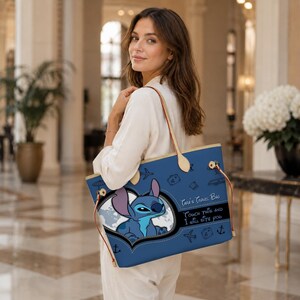 May include: A blue tote bag with a cartoon Stitch design and travel icons. The bag has a light-colored handle and the text "Tara's Travel Bag, Touch this and I will bite you". The bag is carried over the shoulder.