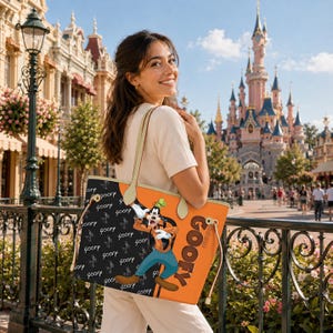 May include: An orange and black tote bag featuring the character Goofy. The bag has a black panel with the word "Goofy" repeated in a pattern. The other panel is orange with the word "Goofy" in large letters and a cartoon image of Goofy.