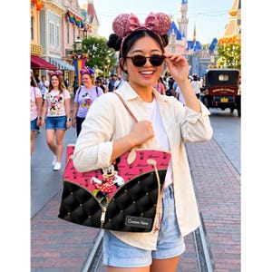 May include: A pink and black tote bag featuring Minnie Mouse. The bag has a quilted black bottom with a zipper design and a pink top with Minnie Mouse graphics. The bag has a custom name tag and is carried by a person wearing sunglasses.