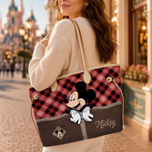 May include: A tote bag with a red and black plaid pattern, featuring a brown pocket with a zipper and the word "Mickey". The bag has a Mickey Mouse graphic and cream-colored handles.