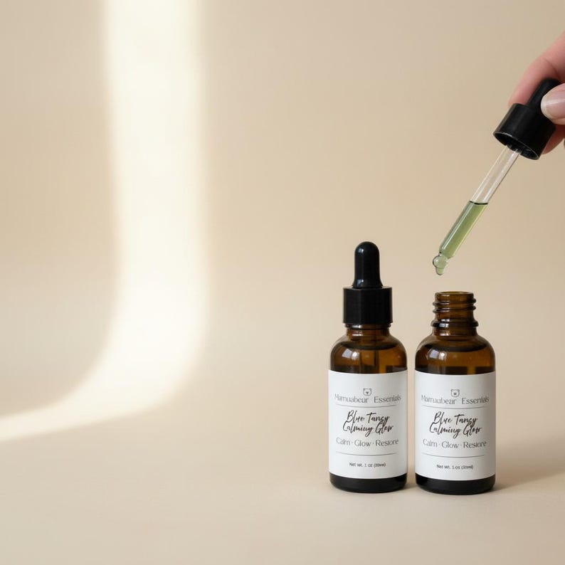 May include: Two amber glass bottles with black droppers, labeled "Blue Tangy Calming Glow" and "Cam-Glow Restore." A dropper dispenses a green liquid. The bottles are on a neutral background, suggesting a skincare product.