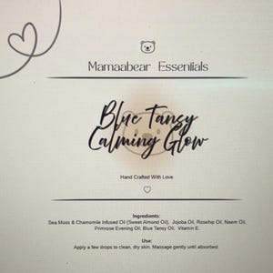 May include: A product label for Mamaabear Essentials. The label features the text "Blue Tansy Calming Glow" in elegant script. Ingredients and usage instructions are listed below. The design includes a heart and a bear icon.