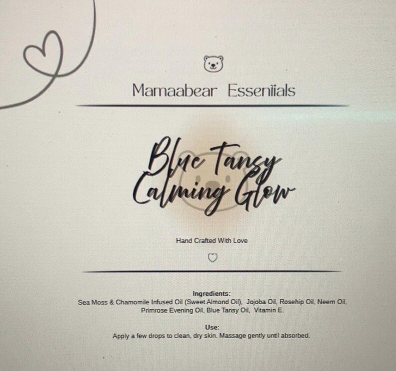 May include: A product label for Mamaabear Essentials. The label features the text "Blue Tansy Calming Glow" in elegant script. Ingredients and usage instructions are listed below. The design includes a heart and a bear icon.