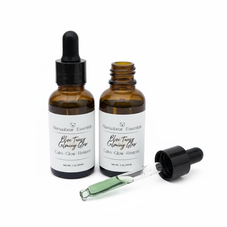 May include: Two amber glass bottles of skincare serum with black droppers. The bottles have white labels with the text "Blue Tangy Calming Glow". One dropper is open, revealing a green liquid. Each bottle contains 1 oz (30ml) of product.
