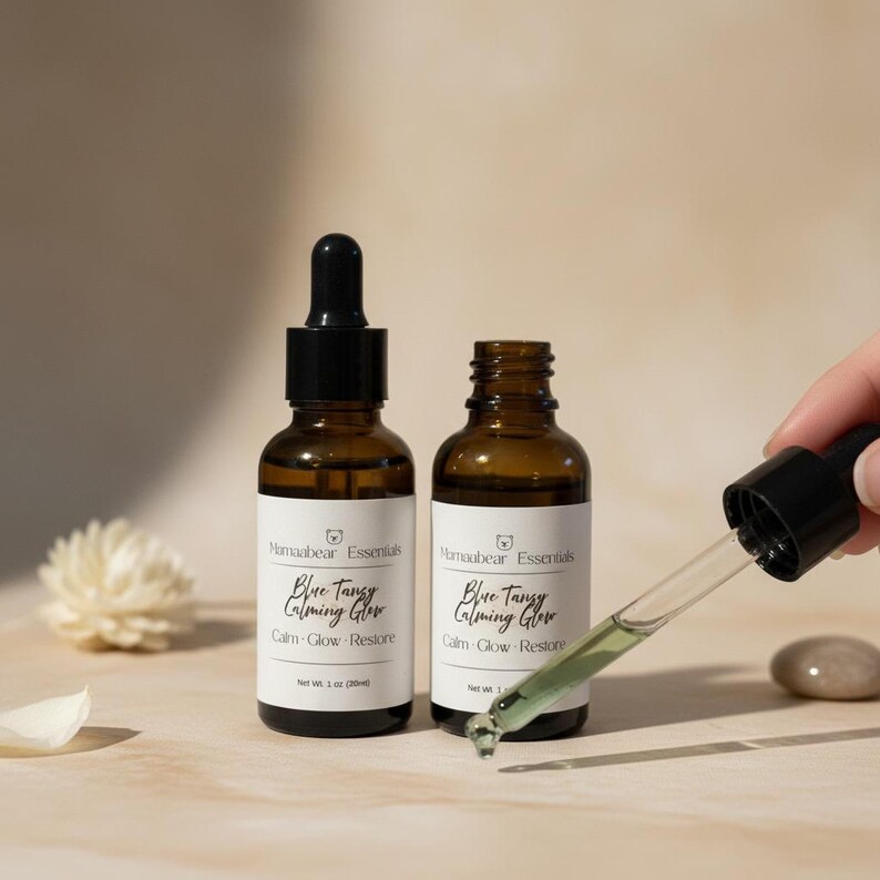 May include: Two amber glass bottles of facial serum with black droppers. The bottles have white labels with the text "Blue Tangy Calming Glow" and "Calm-Glow Restore". A dropper is held up with serum in it. The net weight is 1 oz (30ml).
