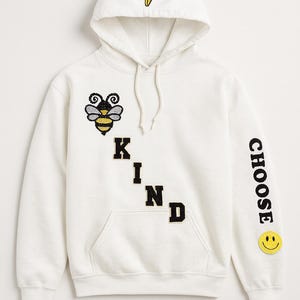May include: White hoodie with a bee and lightning bolt patch. The word "KIND" is spelled out on the front, and the sleeve says "CHOOSE" with a smiley face. The hood has a yellow lightning bolt.