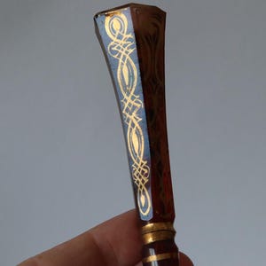 Può includere: Un timbro sigillo decorativo marrone con un design oro e blu. Il timbro ha una forma rettangolare con un motivo dorato dettagliato su sfondo blu. L'impugnatura è di colore marrone scuro con accenti dorati.