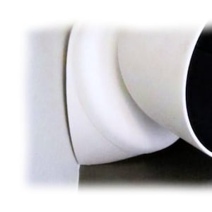 May include: Close-up of a white, curved pipe fitting. The fitting has a smooth, matte finish and a rounded shape. The interior of the pipe is black. The image is well-lit, highlighting the clean lines and form of the object.