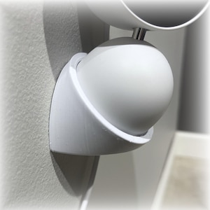 Może przedstawiać: Biała, kulista, regulowana lampa ścienna. Oprawa ma zaokrągloną, kulistą głowicę świetlną i zakrzywiony wspornik przymocowany do ściany. Projekt jest minimalistyczny i nowoczesny.