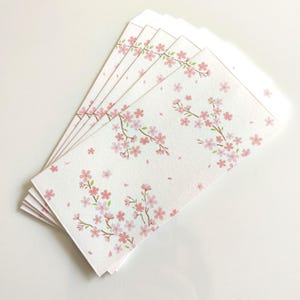 May include: A stack of white envelopes with a delicate pink cherry blossom design. The envelopes feature branches with pink flowers and scattered petals, creating a spring-like aesthetic. The design is repeated across the surface of each envelope.