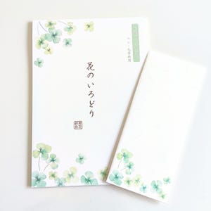 May include: A white stationery set featuring a notepad and a matching envelope, both decorated with watercolor-style green and yellow clover illustrations. The notepad displays Japanese text and a small red seal, with a green rectangular label at the top.