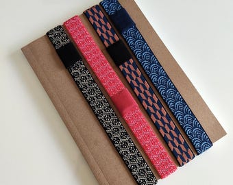 Puede incluir: Cuatro bandas elásticas con patrones distintos dispuestas en diagonal sobre un soporte rectangular de cartón marrón. Los patrones incluyen un estampado geométrico en blanco y negro, un diseño hexagonal rojo, un motivo de flechas azul y marrón, y un patrón de olas azul.