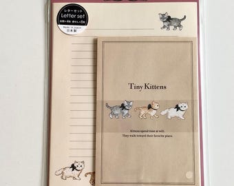 Puede incluir: Un juego de papelería en una funda de plástico transparente que incluye un sobre beige con el texto Tiny Kittens y tres gatitos ilustrados con lazos negros. El papel rayado incluye una pequeña ilustración de un gatito y un lazo.