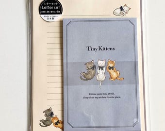 Puede incluir: Un juego de papelería que incluye un sobre azul claro con tres gatitos con lazos negros y el texto Tiny Kittens. El set contiene papel de carta rayado de color crema con ilustraciones de gatitos y una etiqueta circular que indica 4 sobres y 8 hojas.