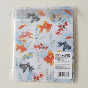 May include: A stationery set in a clear plastic sleeve featuring a watercolor print of orange, black, and white goldfish swimming among green aquatic plants on a light blue background. A white label with black text and a barcode is attached.