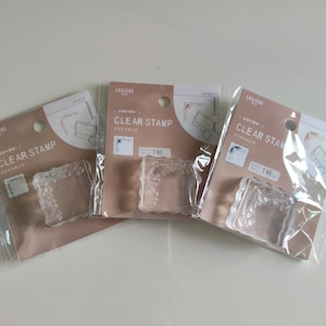 May include: Three clear stamps packaged in individual plastic sleeves with beige cardboard backing. Each package features the text LOUJENE TOKYO and CLEAR STAMP, displaying a corner design illustration and a single clear acrylic stamp inside.