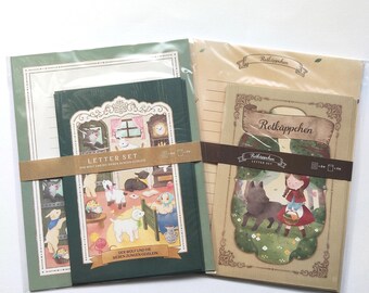 Puede incluir: Dos juegos de papelería en envases de plástico transparente. El conjunto de la izquierda presenta una cubierta verde oscuro con una ilustración de un lobo y siete cabritos. El conjunto de la derecha tiene una cubierta beige con una niña de caperuza roja.