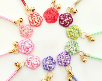 May include: A collection of ten decorative charms arranged in a circle, each featuring a knotted cord flower in various colors including pink, red, purple, green, and lavender, accented with a small gold-toned metal bell and a braided cord strap.