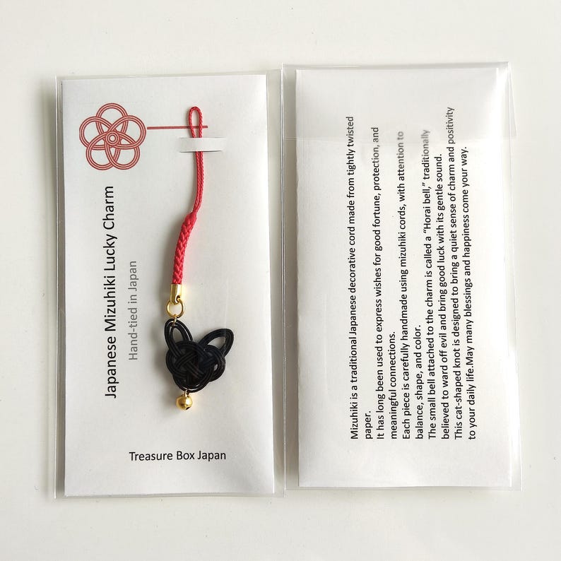 May include: A Japanese Mizuhiki lucky charm featuring a black cat-shaped knot made from paper cord, attached to a red braided loop with a small gold bell. The charm is presented on a white card with the text Japanese Mizuhiki Lucky Charm.