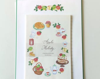 Puede incluir: Un juego de papelería con una hoja blanca de borde verde y una tarjeta color crema. La tarjeta muestra ilustraciones de manzanas, pasteles, juegos de té y una cesta, con el texto Apple Melody y If only this world could be full of love.