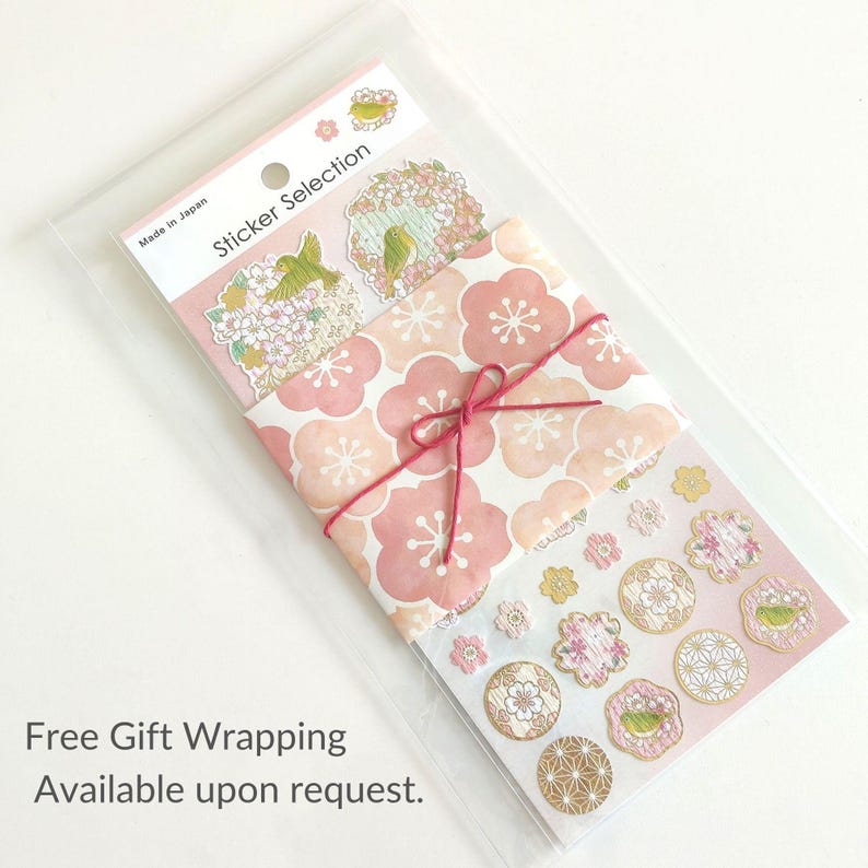 May include: A pack of decorative stickers in a clear plastic sleeve. The header reads Sticker Selection and Made in Japan. The stickers feature pink cherry blossom patterns, small green birds, and geometric gold designs, wrapped in a pink paper band.