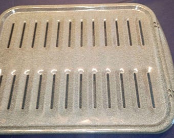May include: A rectangular gray speckled broiler pan insert featuring two parallel rows of vertical ventilation slots. The metal tray has a raised border and small circular perforations on the side edges, designed for draining liquids during cooking.