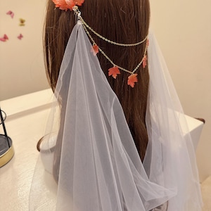 Op de afbeelding: Bruidssieraad met oranje esdoornbladaccenten en een gouden ketting. Het sieraad is bevestigd aan een doorschijnende witte sluier, wat een elegante en etherische uitstraling creëert.