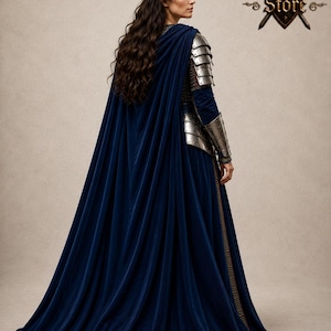 May include: A woman wearing a long, flowing navy blue velvet gown with a matching cape. The gown features silver metal armor on the shoulders and arms. The Medieval Store logo is visible in the upper right corner.