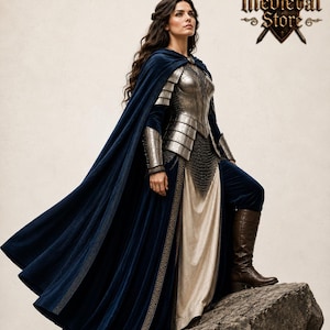 May include: A woman in medieval attire, including a silver breastplate, chainmail, and a flowing navy blue cape. The outfit is completed with brown boots and a cream-colored dress. The image features the "Medieval Store" logo.