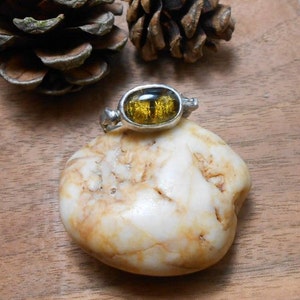 May include: A silver ring featuring a large oval-shaped amber stone. The stone is a deep yellow colour with a golden sheen. The ring is set on a white rock.