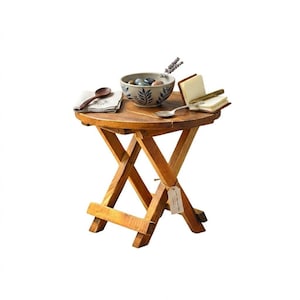 Könnte beinhalten: Kleiner, runder, klappbarer Holztisch mit natürlichem Finish. Auf dem Tisch befinden sich eine Schale mit dekorativen Steinen, ein Löffel, eine Serviette, ein kleines Notizbuch und ein Lavendelzweig. Der Tisch hat einen Durchmesser von ca. 46 cm.
