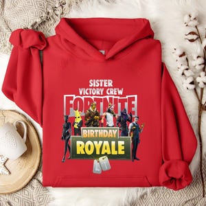 Pu&ograve; includere: Una felpa con cappuccio rossa con la scritta "SISTER VICTORY CREW FORTNITE BIRTHDAY ROYALE" e grafica di personaggi. La felpa ha una tasca a marsupio e un cappuccio con coulisse. Il design presenta personaggi del videogioco Fortnite.