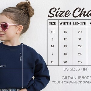 A young girl wearing a navy blue crew neck sweatshirt and pink heart-shaped sunglasses, with a size chart and US sizes (IN) for the sweatshirt.