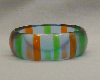 May include: A colorful, striped bangle bracelet. The bracelet features vertical stripes of orange, green, and white. The bracelet is made of a translucent material.