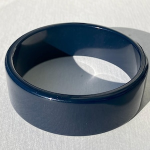 May include: A dark blue plastic bangle bracelet. The bracelet is smooth and shiny.