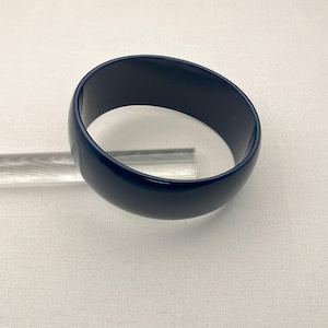 May include: A dark blue plastic bangle bracelet. The bracelet is smooth and shiny.