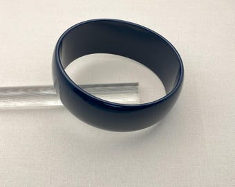 May include: A dark blue plastic bangle bracelet. The bracelet is smooth and shiny.