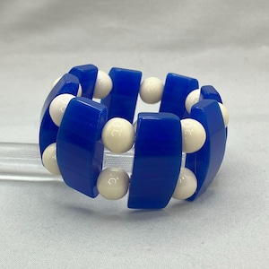 May include: A blue and white plastic bracelet with alternating blue and white beads. The blue beads are rectangular and the white beads are round.