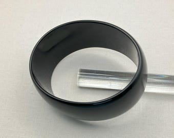 May include: A black plastic bangle bracelet. The bracelet is smooth and shiny.