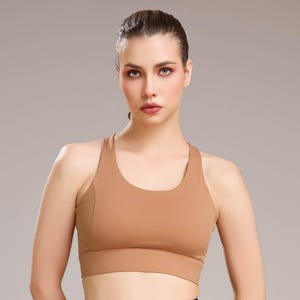 May include: A tan-colored sports bra with a scoop neckline and racerback design. The bra is made of a smooth, seamless material and provides medium support. The image shows the bra on a person.