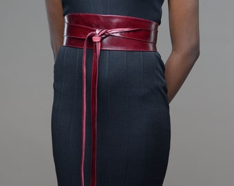 May include: A burgundy leather belt with long ties. The belt is wrapped around a black dress and tied in a knot at the front.