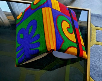 May include: A colorful, geometric patterned notebook with a blue, green, yellow, and red design. The notebook has a black elastic band closure.