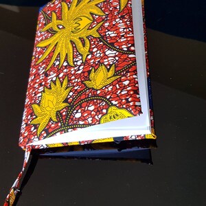 Può includere: Un quaderno con motivo rosso, giallo e bianco con un cinturino nero. Il quaderno è aperto e le pagine sono vuote.