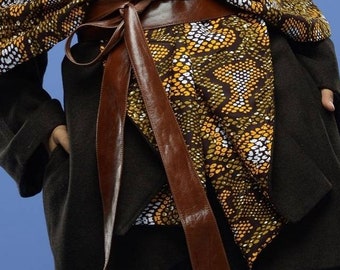 May include: A brown leather belt with a large bow tied in the front. The belt is worn over a brown and yellow patterned fabric.